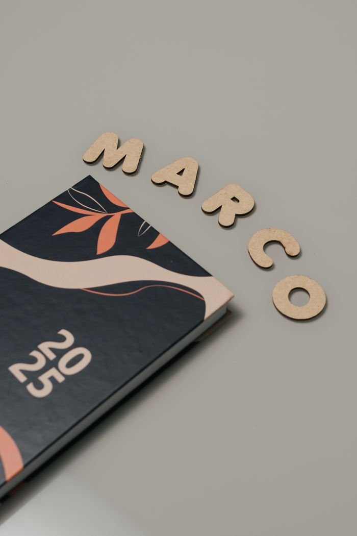 Top view of a 2025 planner with wooden letters spelling 'Marco' on a neutral background.