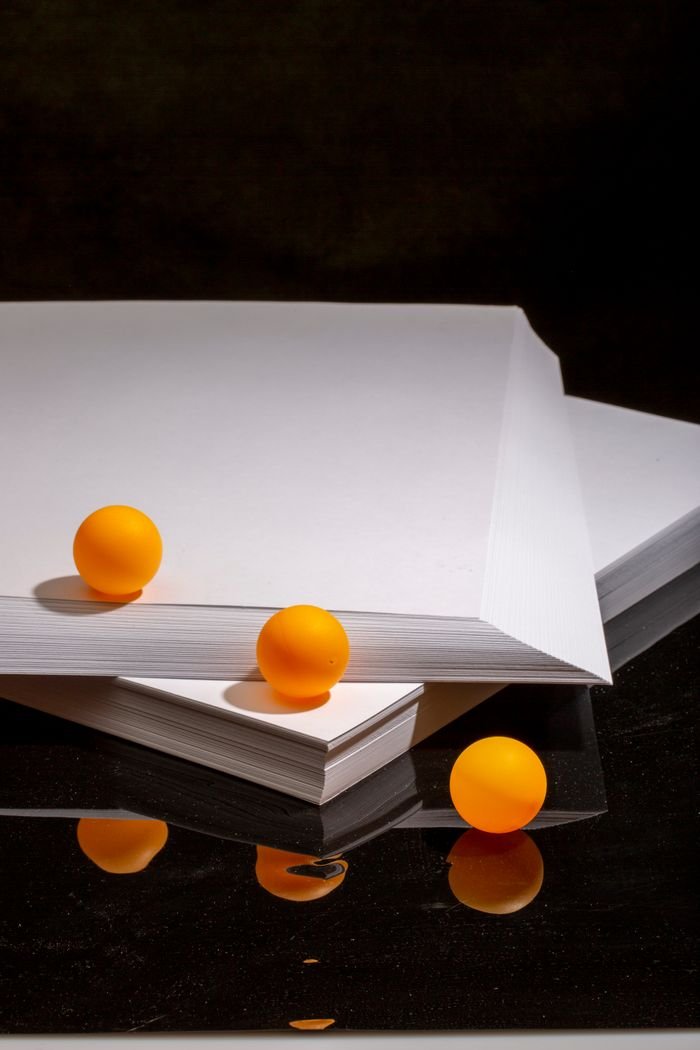 Vivid orange balls arranged on white paper against a dark background, featuring reflections.