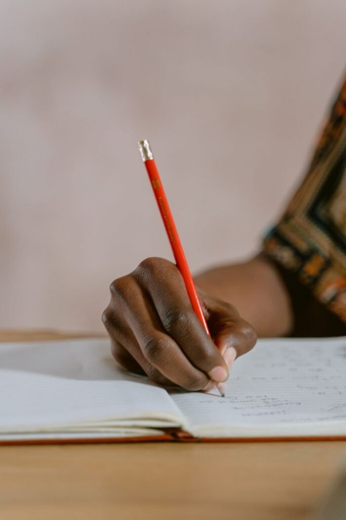 Mastering the First Impression: Your intriguing post title goes here A person writing in a notebook with a red pencil, focusing on the hand's detail.