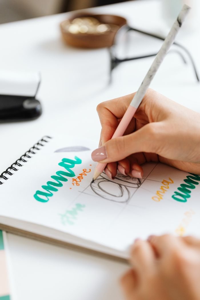A person sketching creative designs in a notebook with a pencil, showcasing hands-on artistic expression.